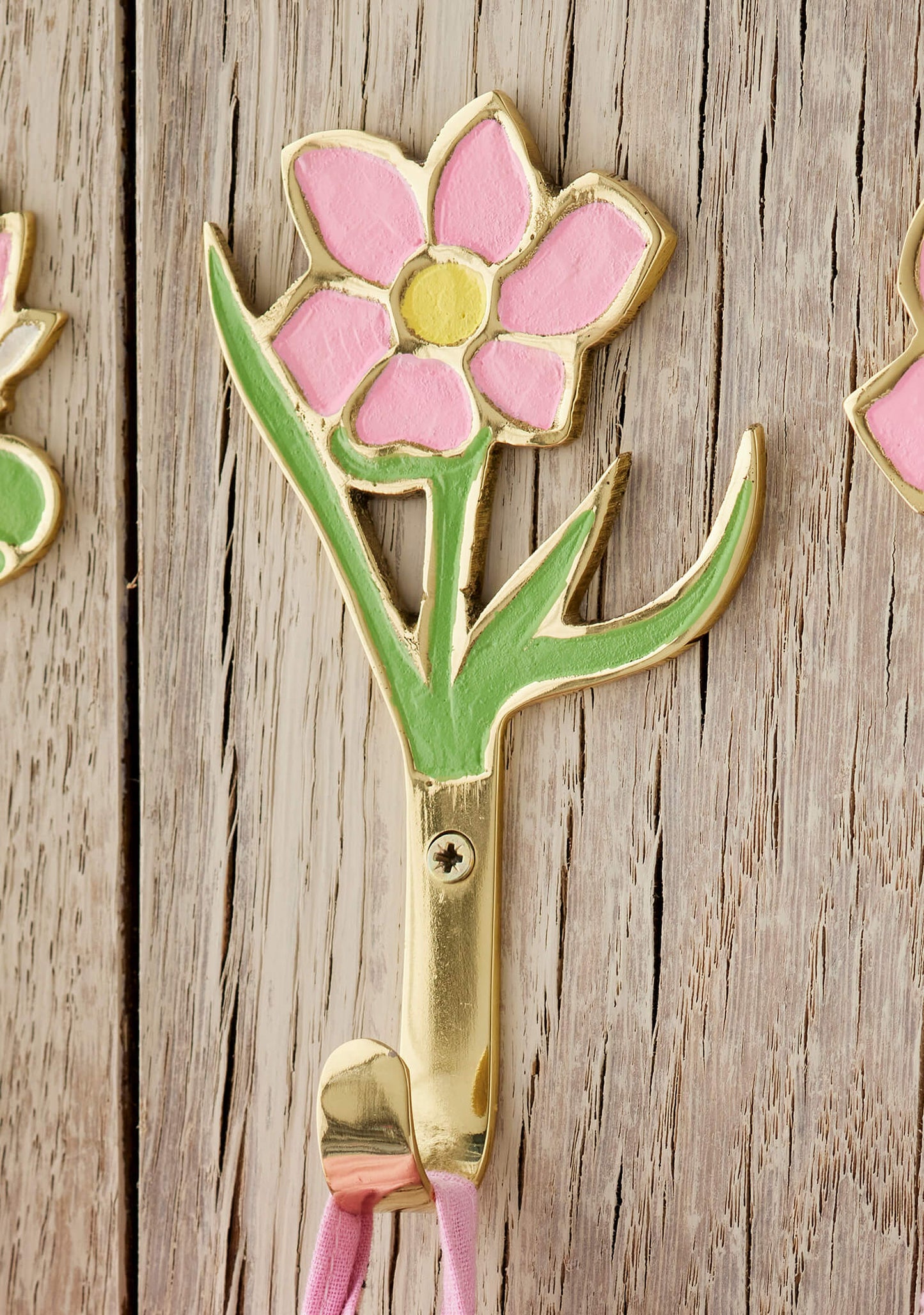 Decorative brass wall hook shaped like a pink flower on a wooden surface