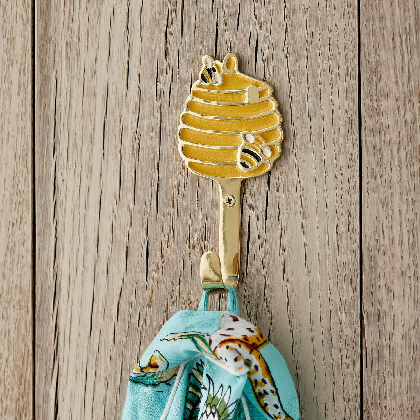 Gold honeycomb shaped hook with a colorful towel on a wooden background. beehive brass wall hook
