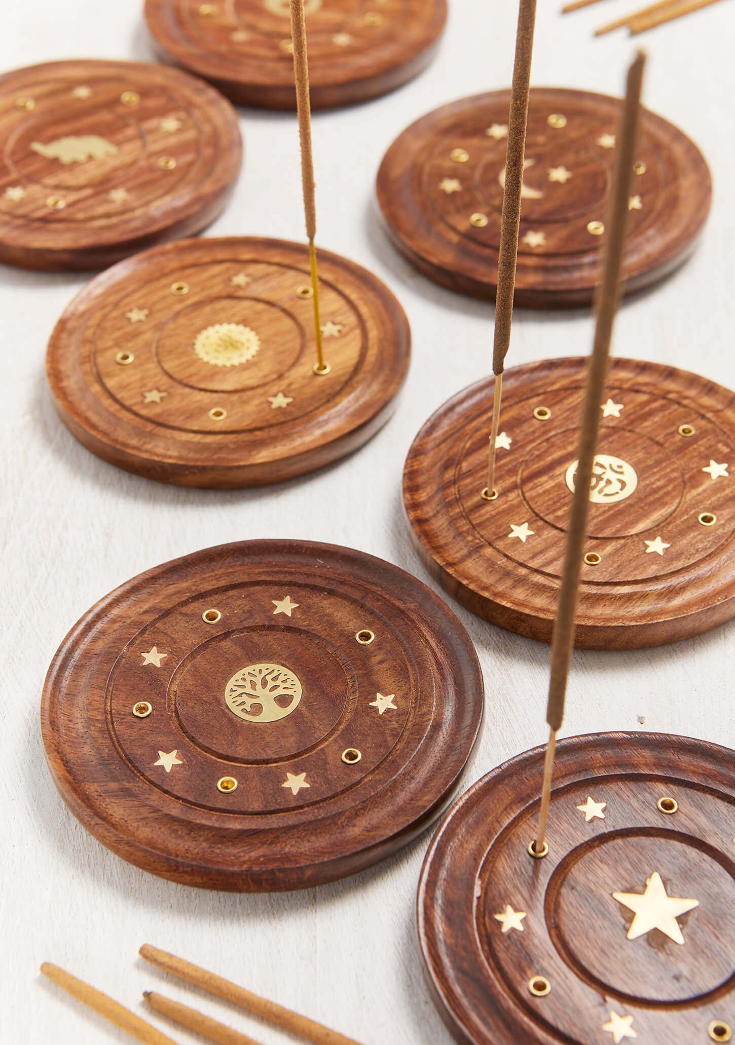 Five incense sticks burning simultaneously in a round brass and wood holder, creating a plume of smoke for a large room meditation session.