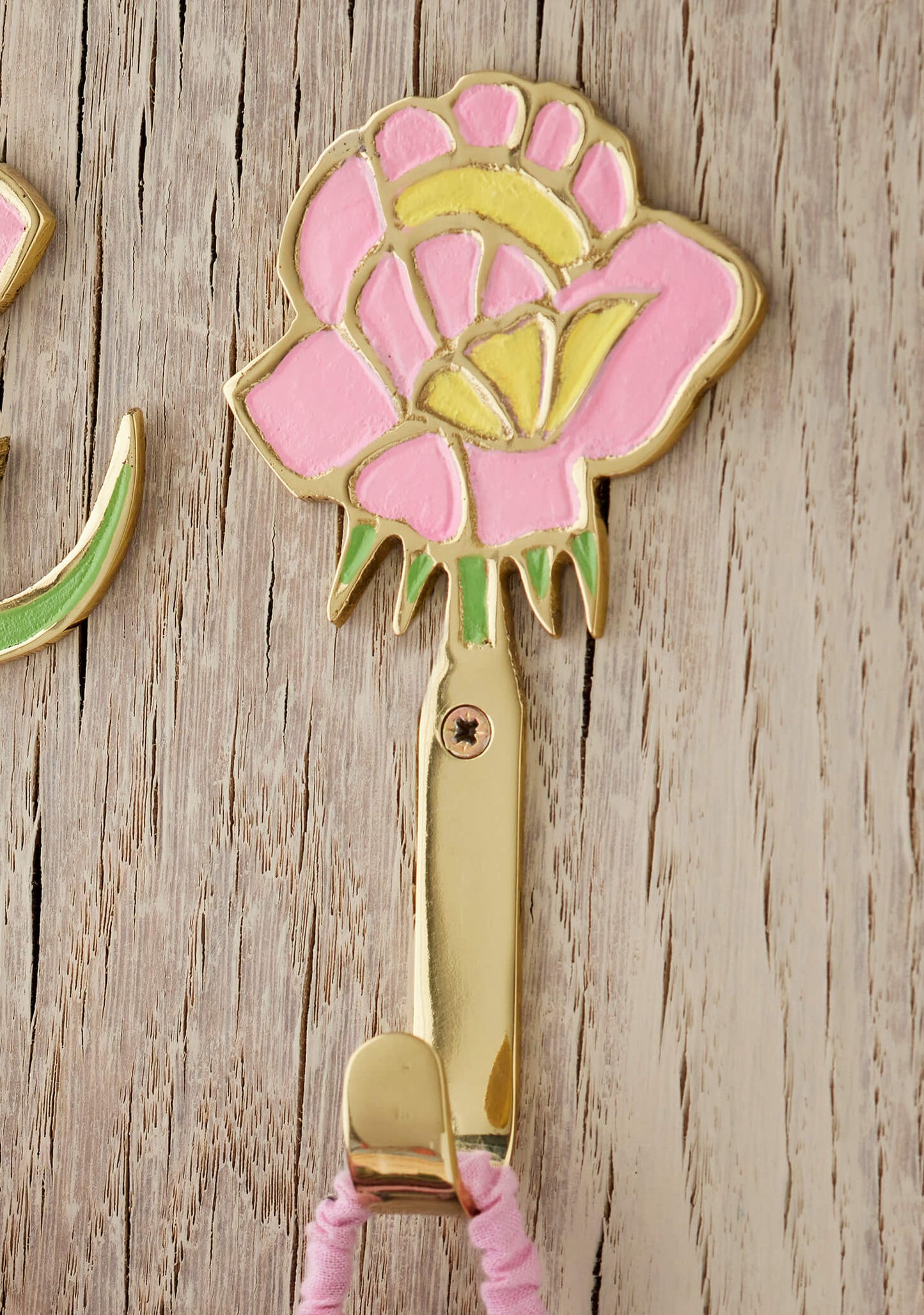 Decorative brass wall hook with pink flower design on a wooden surface