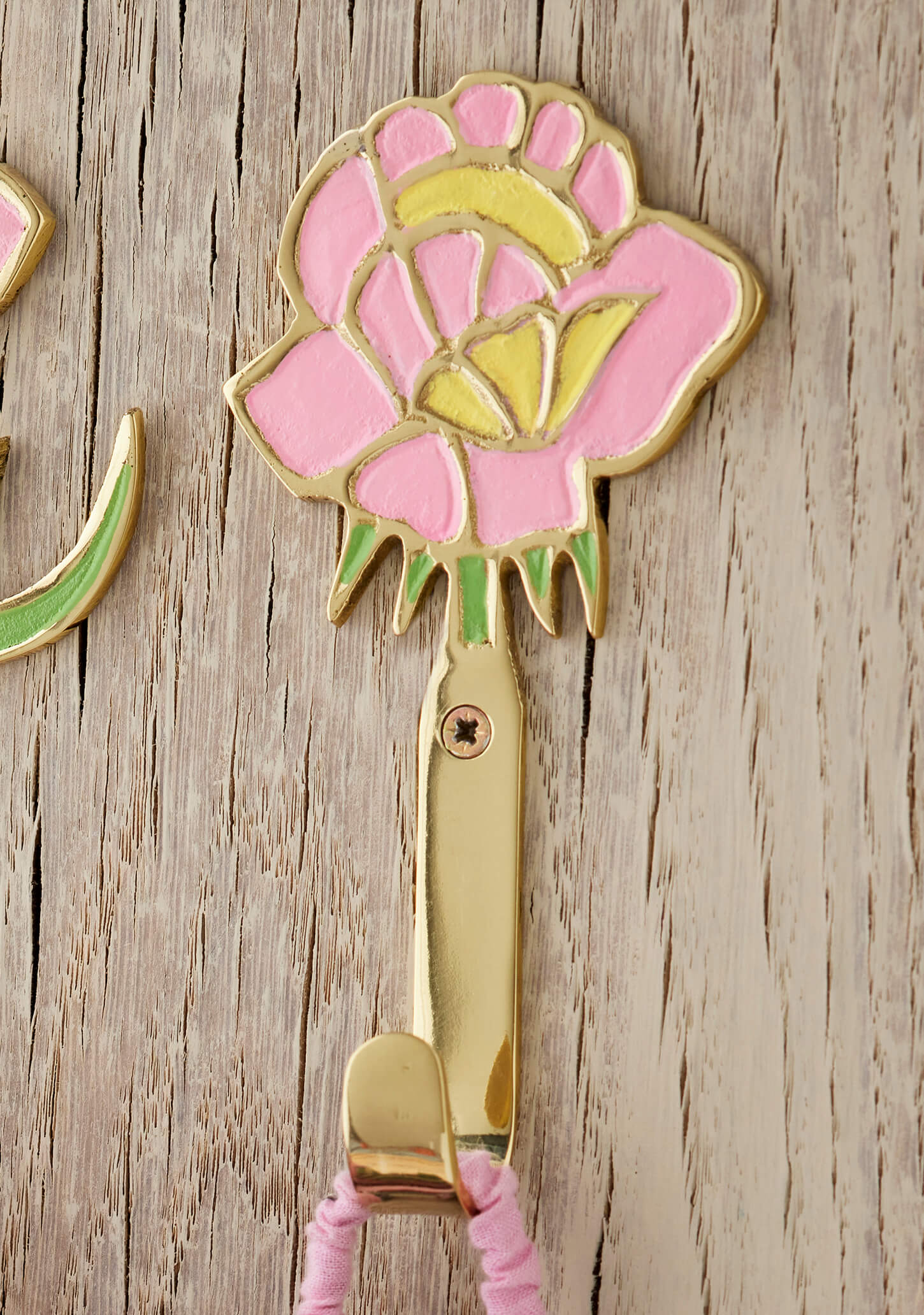 Decorative brass wall hook with pink flower design on a wooden surface
