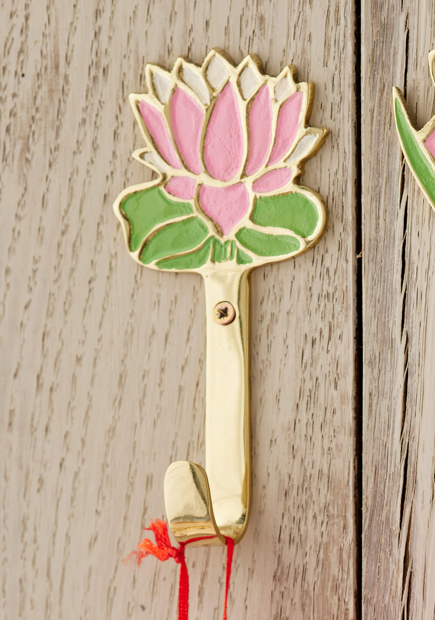 Decorative brass wall hook with pink lotus design on a wooden surface