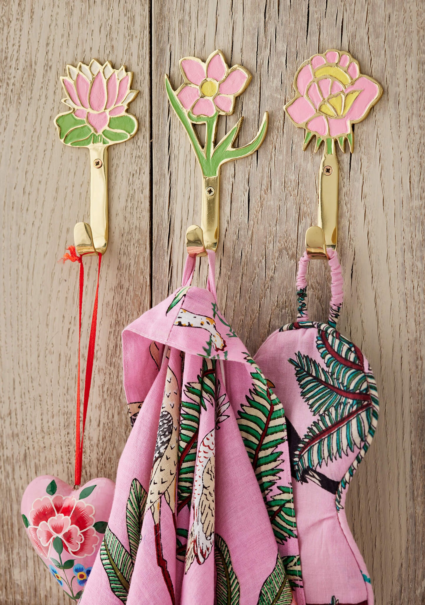 Floral patterned hooks on a wooden wall with pink scarves hanging from them.