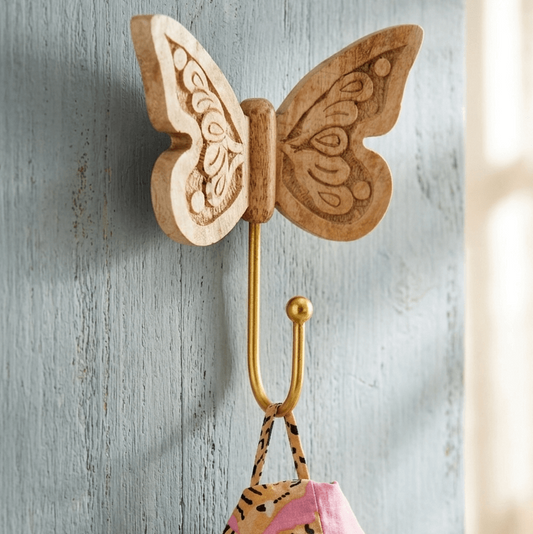 Wooden butterfly shaped sustainable wall hook with a colorful bag hanging from it on a textured gray wall. 