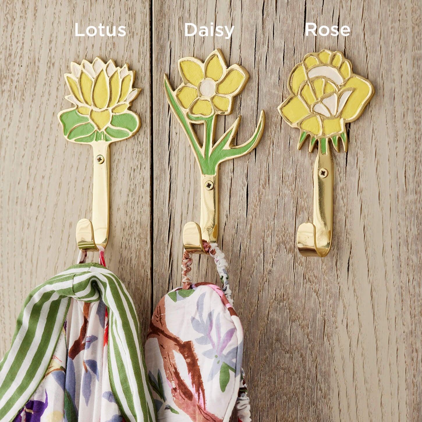 Three yellow flower themed wall hooks labeled 'Lotus', 'Daisy', and 'Rose' on a wooden surface with scarves hanging from them.