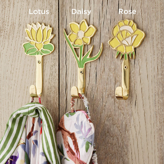 Three yellow flower themed wall hooks labeled 'Lotus', 'Daisy', and 'Rose' on a wooden surface with scarves hanging from them.