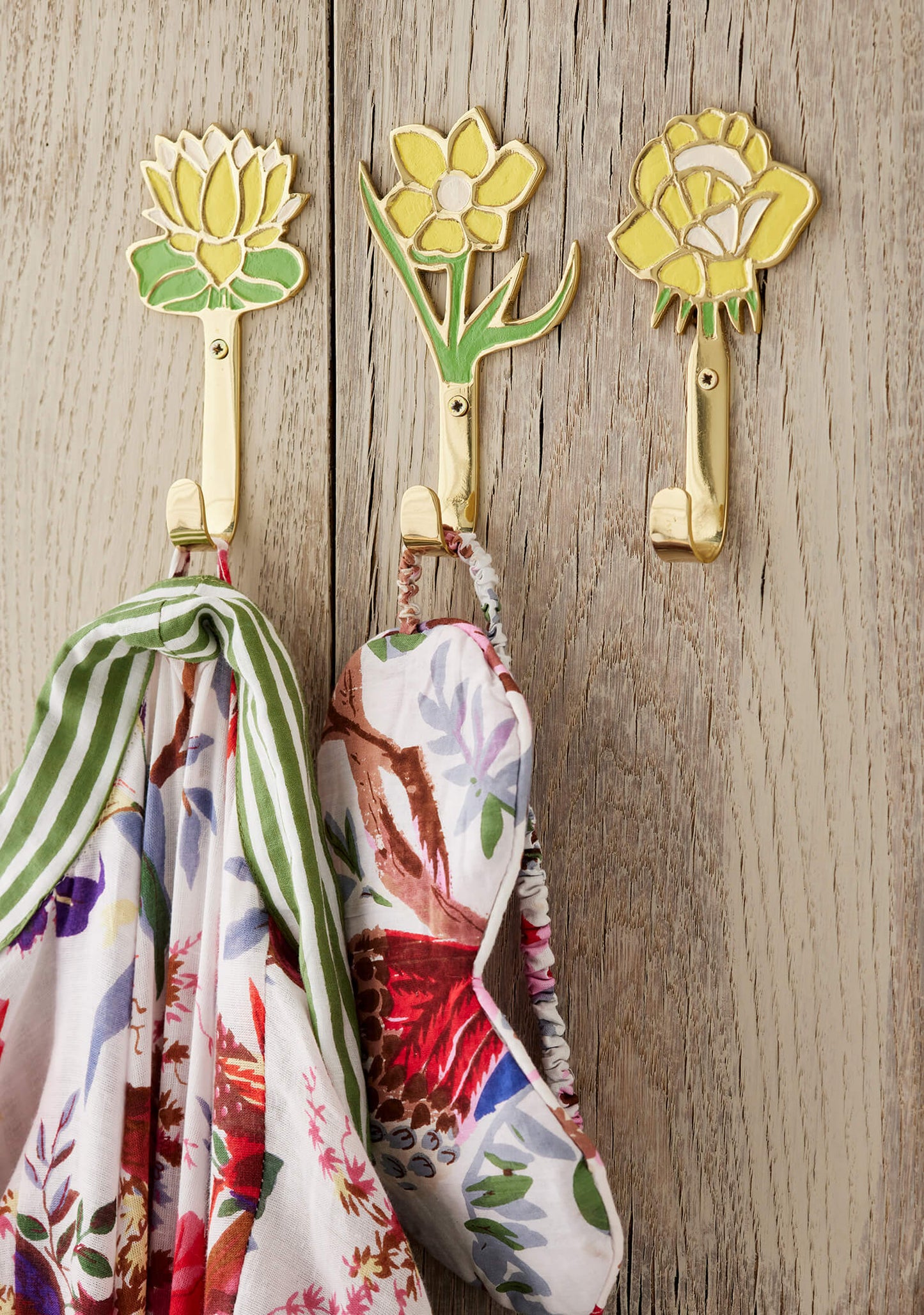 yellow flower patterned hooks on a wooden wall with scarves hanging from them.